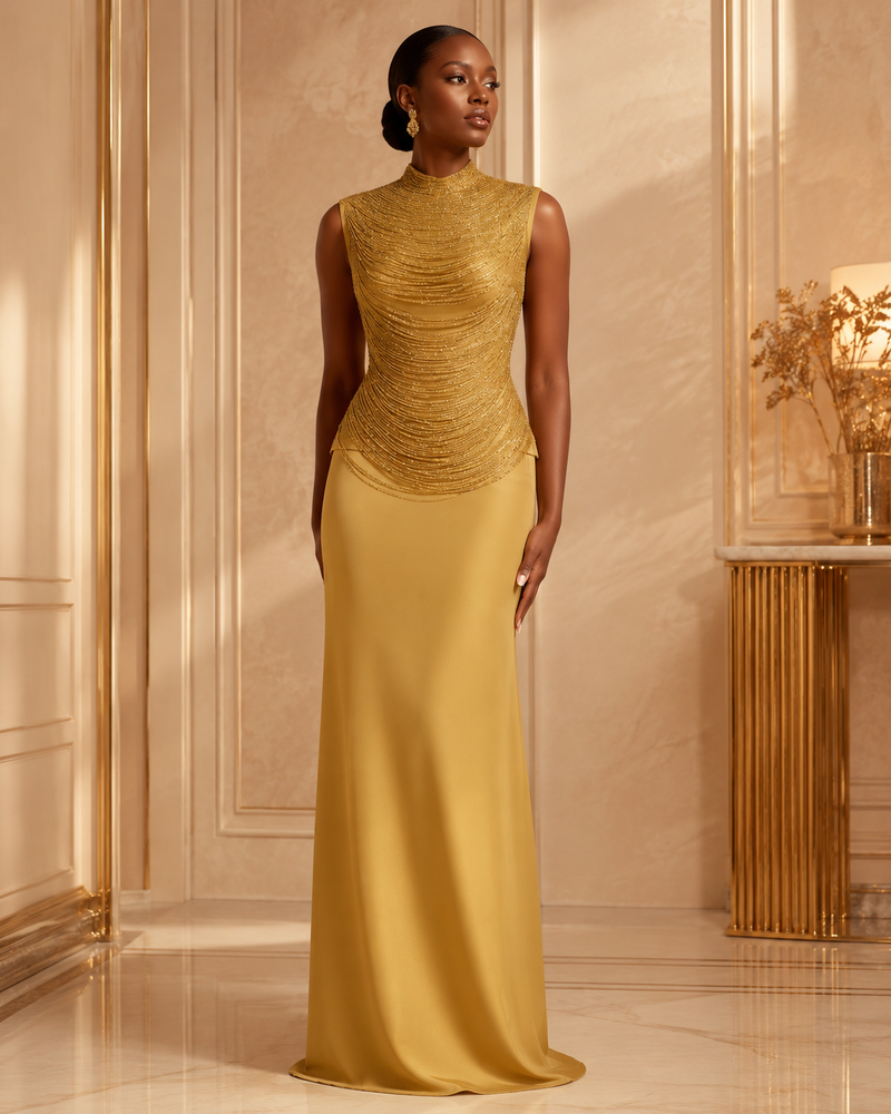 A woman stands in a luxurious cream-colored room wearing a floor-length evening gown. The dress features a textured, ruched gold bodice with a high mock neck and sleeveless design, transitioning into a smooth, flowing satin-like golden skirt.