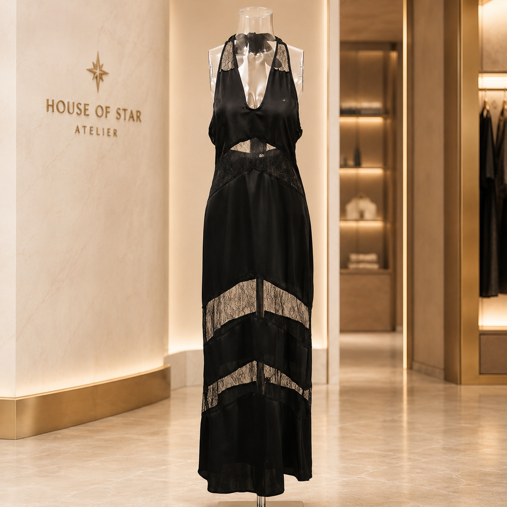 A black satin halter maxi dress with sheer lace panels and a cutout waist, displayed on a mannequin in a luxury boutique interior with 'HOUSE OF STAR ATELIER' on the wall.