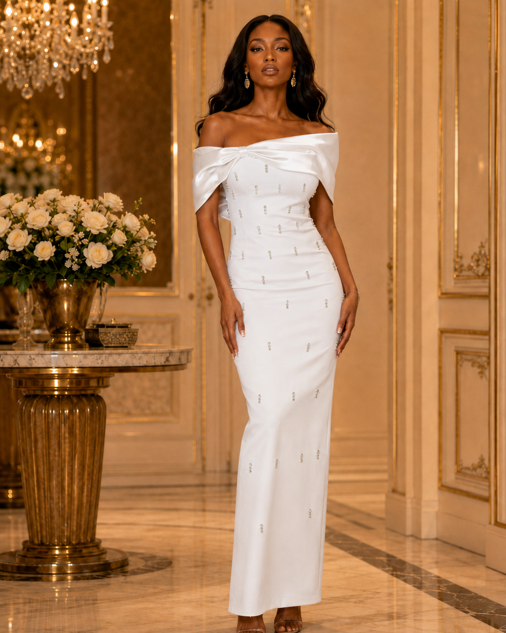 A woman models an off-the-shoulder white satin gown with small gold embroidered details, standing in an elegant, luxurious interior with gold walls and a marble floor.
