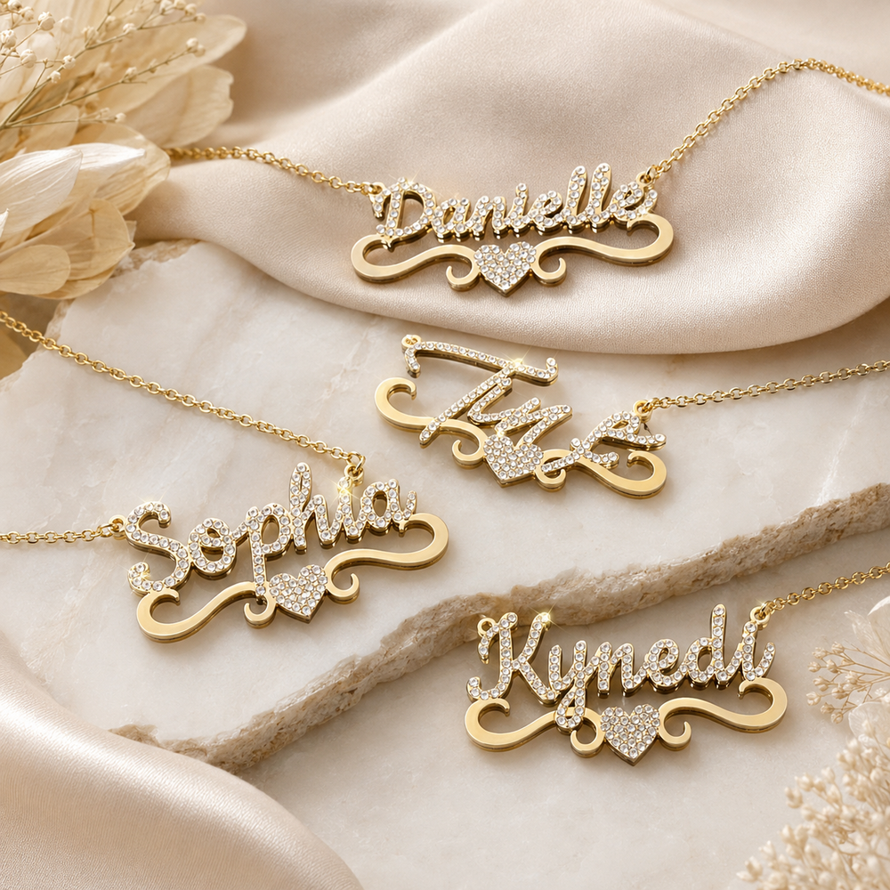 Personalized gold-tone name necklaces with crystal heart details on marble