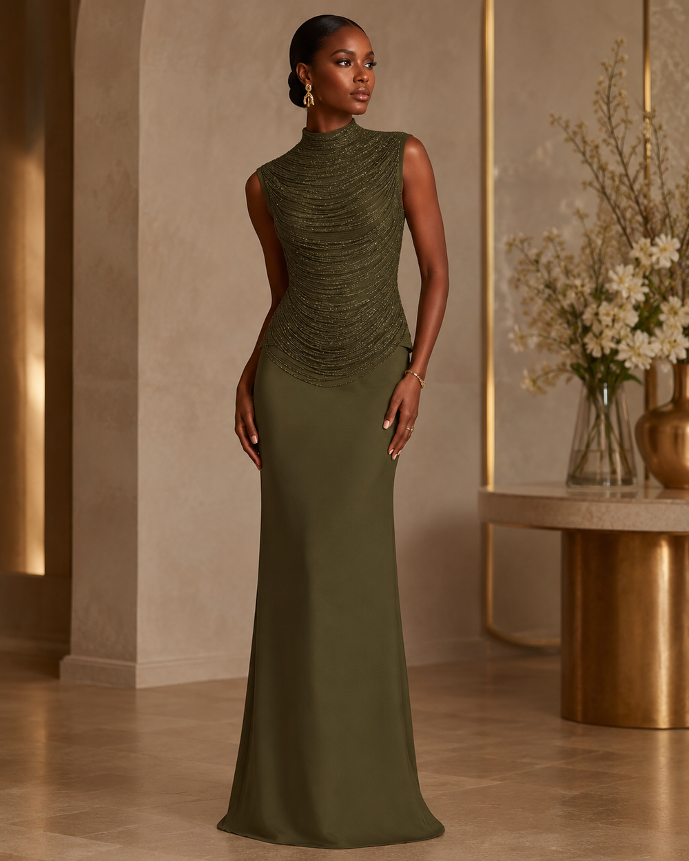 A woman models a sleeveless, high-neck floor-length gown in olive green, standing in a luxurious interior setting with warm beige walls and gold-toned furniture.