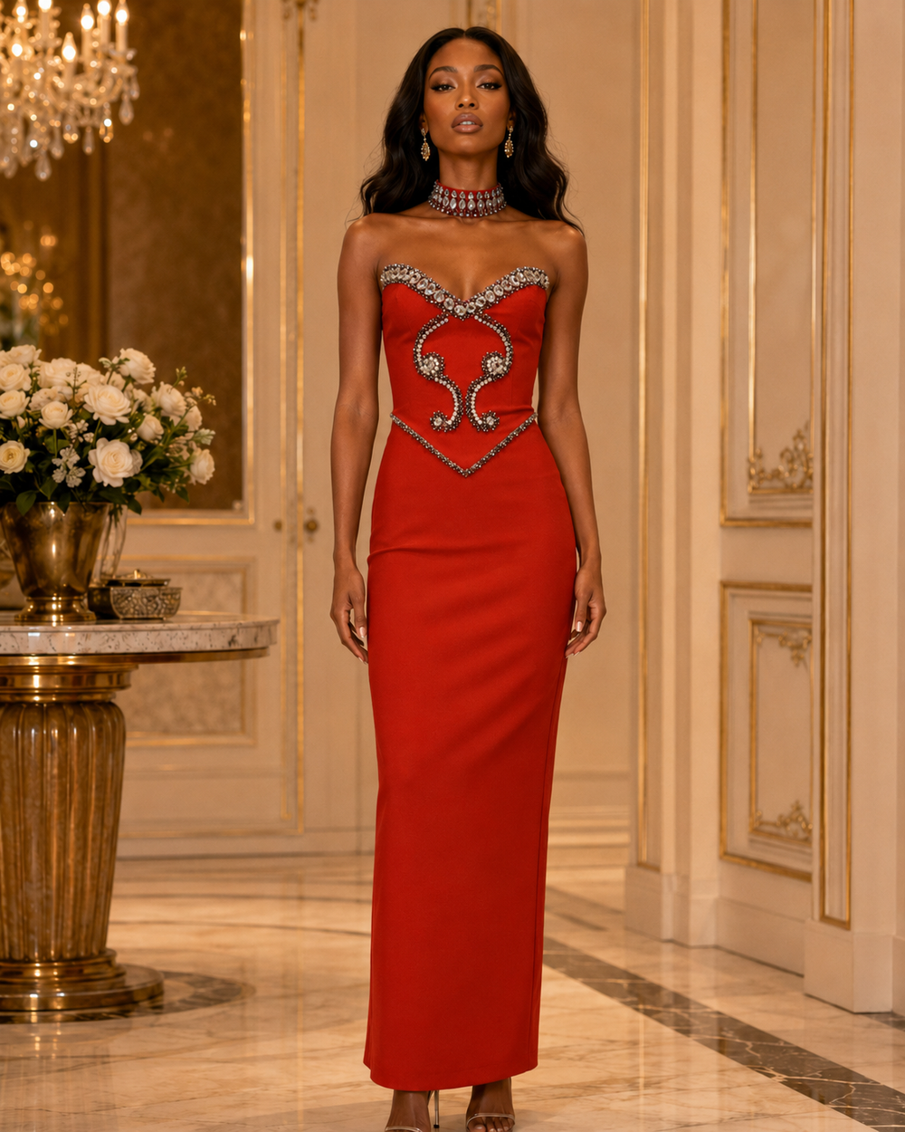 A woman models a strapless red evening gown with a sweetheart neckline and ornate silver embellishments on the bodice, set in an elegant, luxurious interior hallway with gold-trimmed walls and a marble floor.
