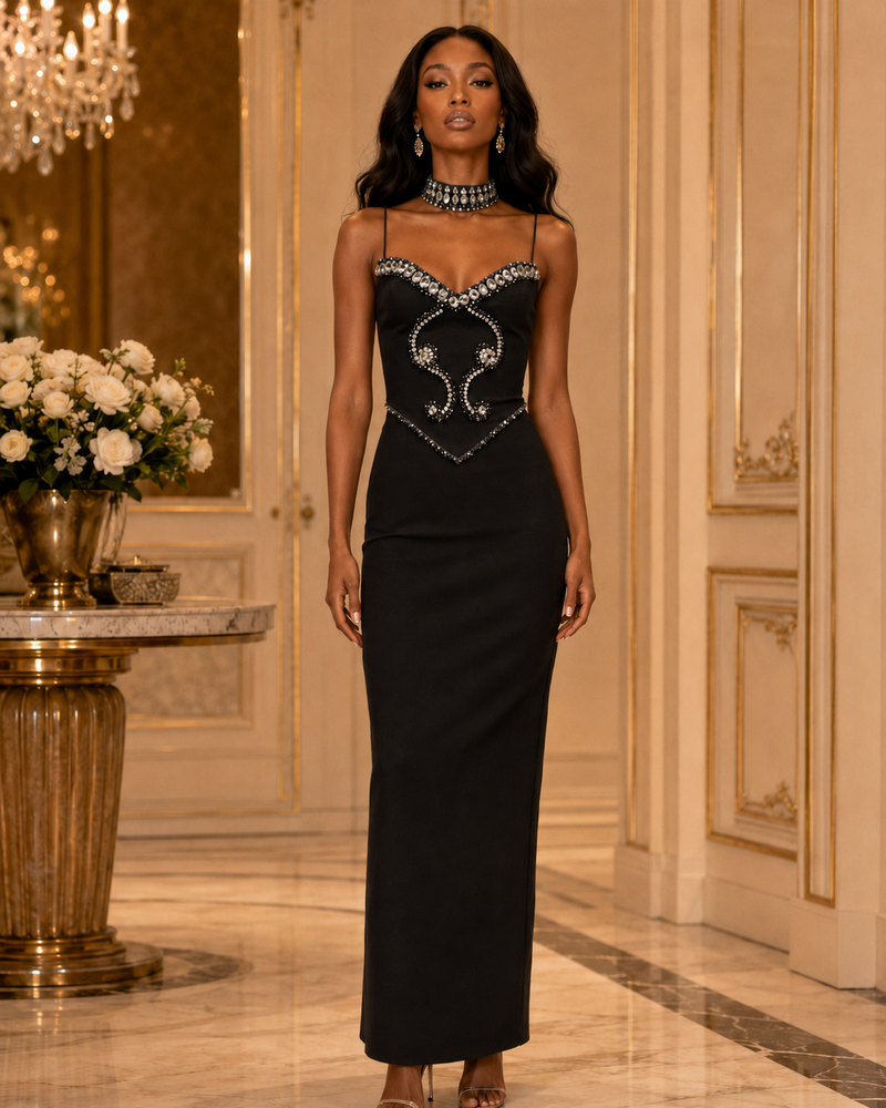 A woman models a strapless black evening gown with a sweetheart neckline and ornate silver embellishments on the bodice, set in an elegant, luxurious interior hallway with gold-trimmed walls and a marble floor.