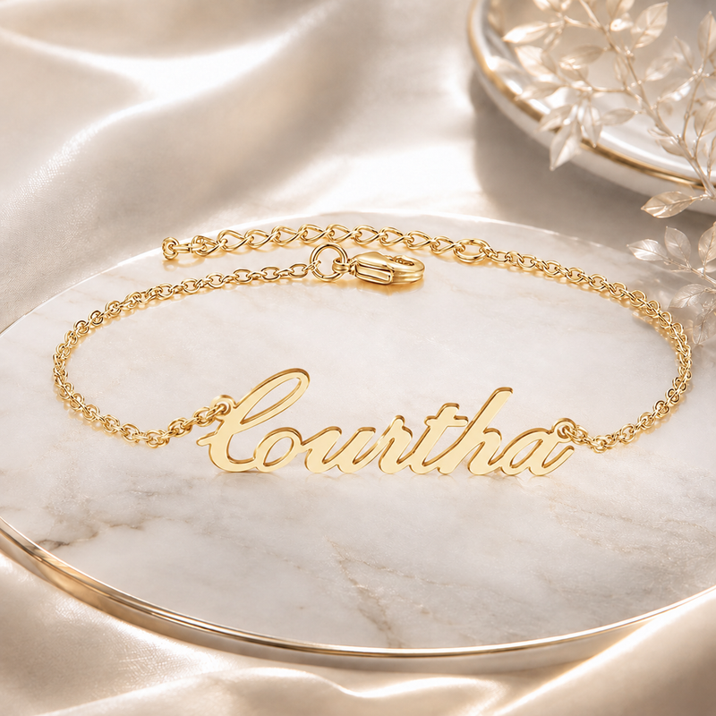 Personalized gold script name bracelet displayed on ivory satin
